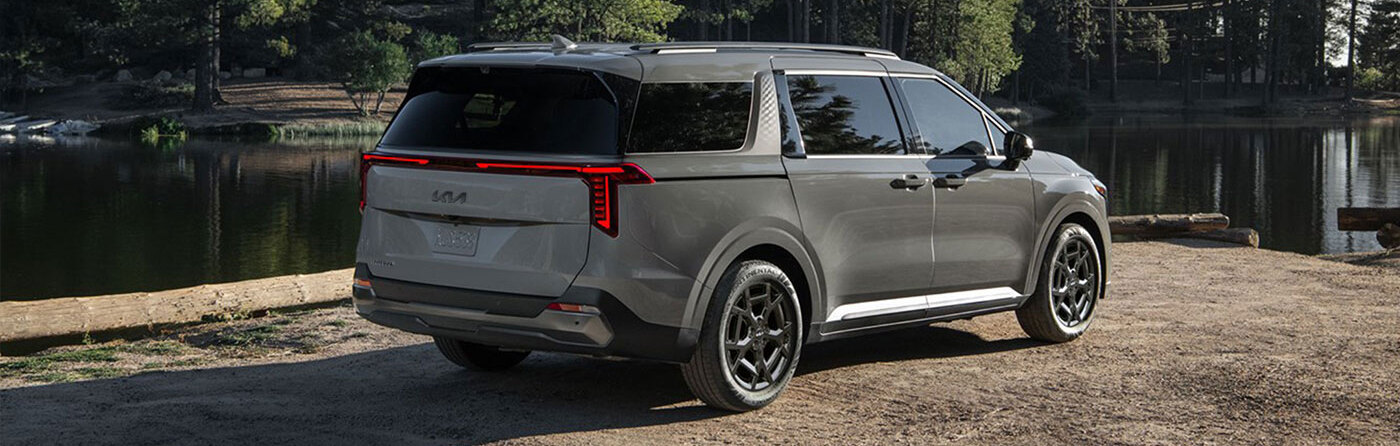 Exterior rear shot of 2026 Kia Carnival parked on gravel road in daylight.