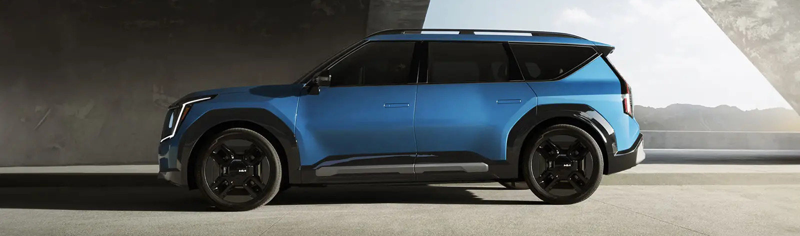 Exterior shot of 2026 Kia EV9 driving on road during daylight.
