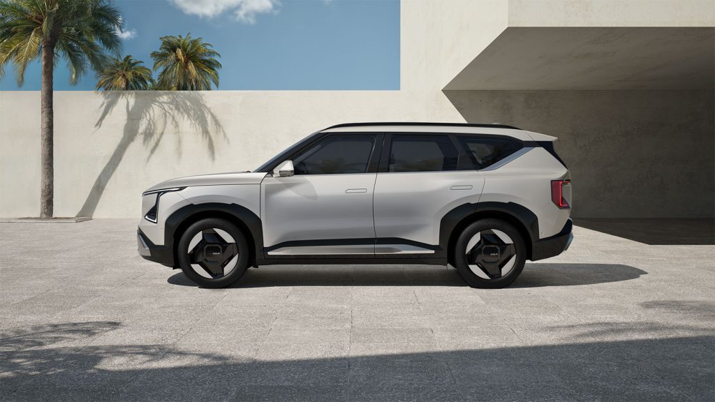 The all-new Kia EV5 side view parked in front of a very modern building with a palm tree.