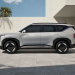 The all-new Kia EV5 side view parked in front of a very modern building with a palm tree.