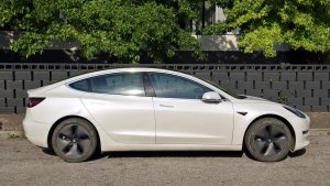 Side view of a white tesla parked against a dark fence. 