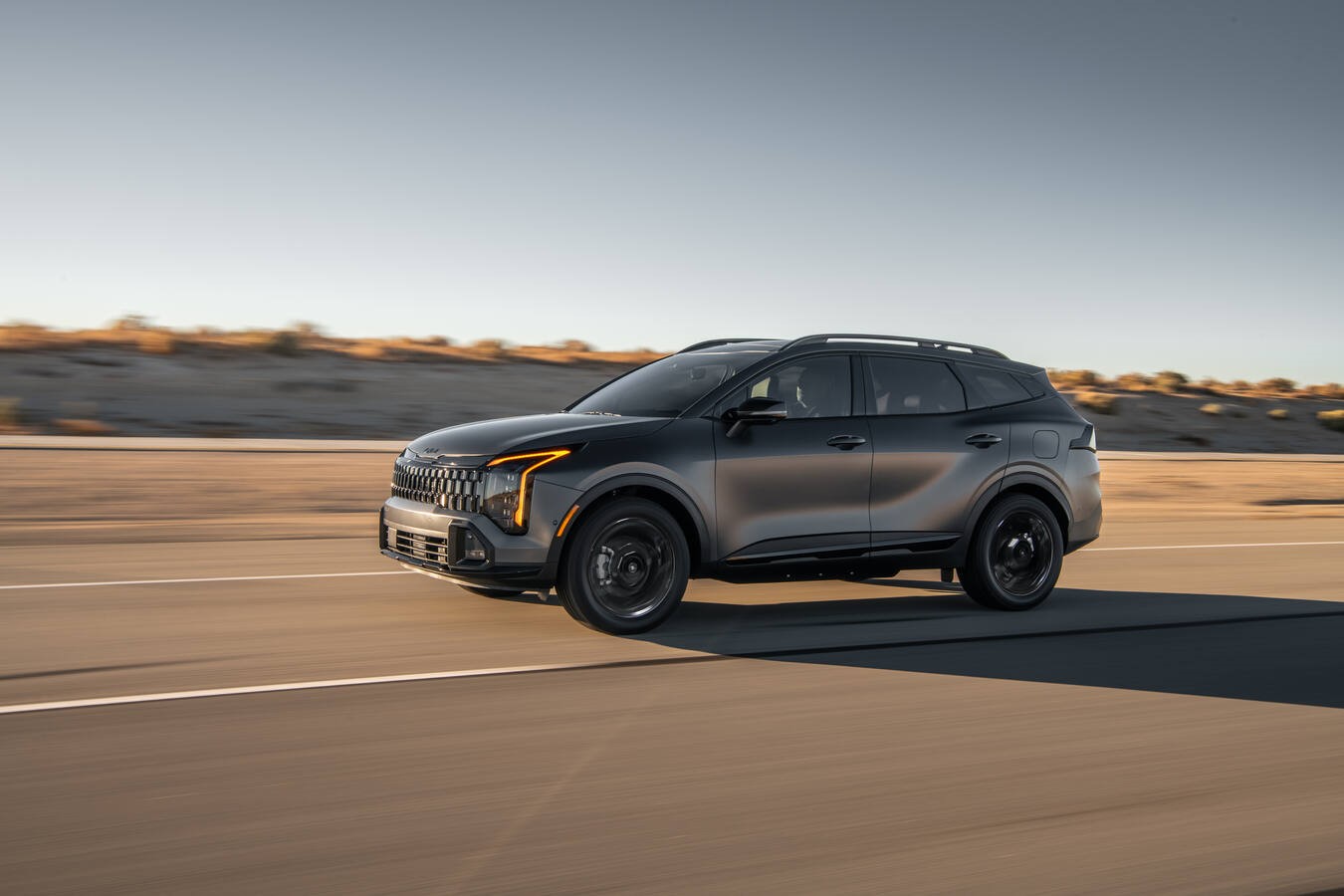 A 2026 Kia Sportage PHEV is driving down the highway at speed with the backgroud blurred. 