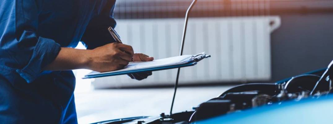 technician inspecting vehicle while holding clipboard