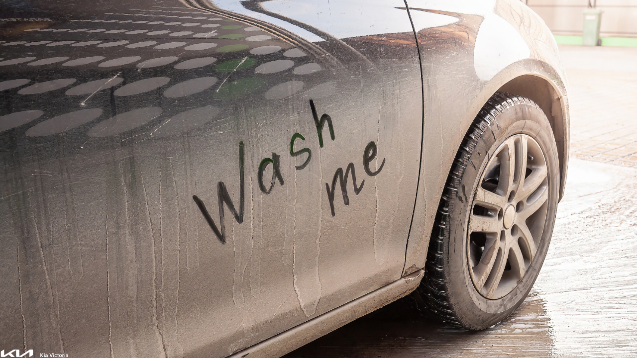 Dirty black car with “WASH ME” written in dust on the side panel after winter driving